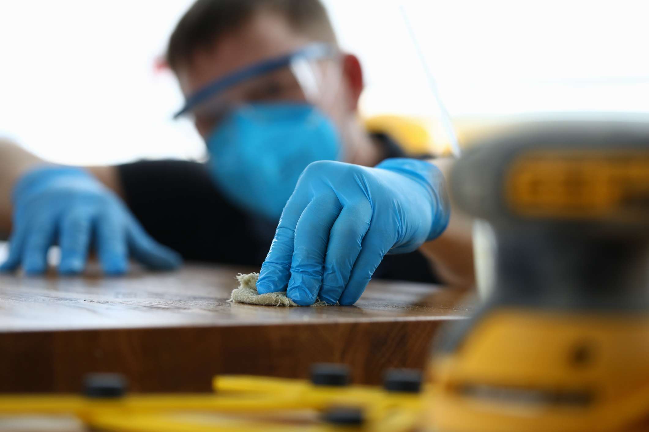 Carpenter in gloves cleans polishes wooden surface